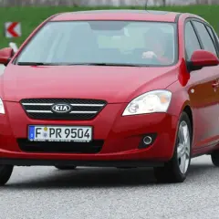 Czerwony Kia Ceed 1.6 CRDi na drodze, z kierowcą za kierownicą.