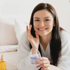 Donna sorridente applica crema viso, scoprendo i benefici di un siero probiotico per una pelle sana e luminosa.