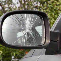 Specchietto rotto dell'auto, con il vetro frantumato in mille schegge che riflettono la luce.