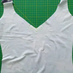 A light blue garment with a deep v neck neckline, trimmed with a delicate zigzag stitch, lies on a green cutting mat.