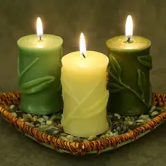 Tres velas verdes encendidas en un plato de mimbre con piedras. Encender velas en casa es malo, pero estas lucen tranquilas.