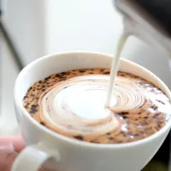 Barista wlewa mleko do kawy, tworząc wzór latte art.