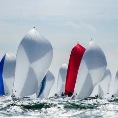Regata con vele gonfie, bianche, blu e rosse. Le barche della j class solcano le onde agitate in una competizione avvincente.