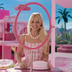 Margot Robbie als Barbie in ihrem pinken Traumhaus, lächelnd durch einen Spiegel.