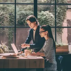 Mężczyzna i kobieta pracują przy laptopie przy biurku, za oknem zieleń.