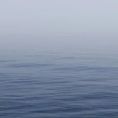 Un mar azul y tranquilo, con una bruma suave que difumina el horizonte. Un lugar perfecto para soñar con el mar azul y tranquilo.