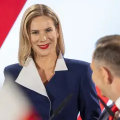 Kobieta w granatowej marynarce z białym kołnierzem uśmiecha się do mężczyzny.