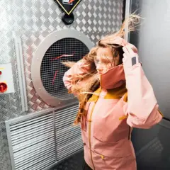 Dziewczyna w kurtce z materiału Gore-Tex co to jest, testuje jej odporność na wiatr w specjalnej komorze.