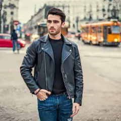 Młody mężczyzna w skórzanej kurtce i jeansach, gotowy się ubrać na imprezę w stylu lat 90. Moda uliczna.