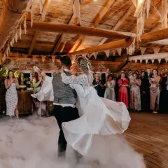 Para młoda tańczy na weselu w dymie. Goście obserwują ich taniec, zastanawiając się, ile trwa wesele.