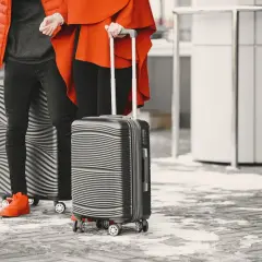 Dwie osoby w pomarańczowych kurtkach stoją z walizkami na zimnym, zaśnieżonym chodniku.