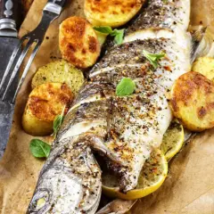 Trota salmonata al forno, dorata e saporita, servita con patate arrosto e limone. Un piatto invitante pronto da gustare.