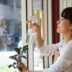 Mujer aplicando spray limpiador en ventana, parte de trucos para limpiar la casa a fondo.