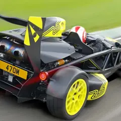 Ariel Atom na torze wyścigowym, z kierowcą w kasku, żółtymi felgami i czarnym spojlerem.