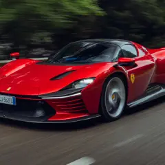 Czerwone Ferrari Daytona SP3 pędzi po krętej drodze, otoczone rozmytą zielenią drzew.