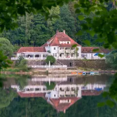 Biały hotel z czerwonym dachem nad spokojnym jeziorem, odbijający się w wodzie.