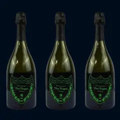 Trzy butelki szampana Dom Pérignon Vintage Brut w ciemnozielonych butelkach z czarnymi kapsułami i zielonymi etykietami.