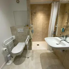 Salle de douche pmr avec WC adapté, barre d'appui, lavabo et douche à l'italienne. Confort et sécurité assurés.