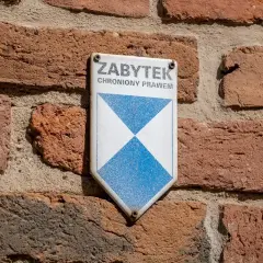 Tabliczka "Zabytek chroniony prawem" na ceglanej ścianie. Może być potrzebna do wypełnienia wzoru wniosku o wykreślenie z gminnej ewidencji zabytków.