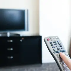 Dłoń naciska przycisk na pilocie od telewizora.