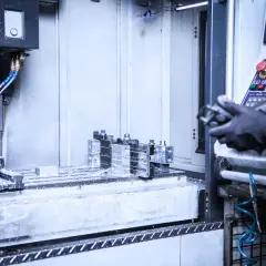 Precyzyjne wiercenie w metalu na maszynie CNC. Chłodziwo rozpryskuje się podczas obróbki. Operator w rękawicach steruje procesem.