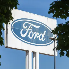 Großes Ford-Logo auf einem Schild, umgeben von grünen Blättern. Vielleicht ein Zeichen für eine neue Ära oder eine ford abfindung.