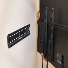 Hands carefully lift a TV, showing how to remove TV from wall mount. The wall bracket is visible.
