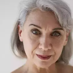Primo piano di una donna con capelli grigi e pelle matura, che mostra i segni del tempo con grazia.