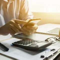 Dłoń trzyma smartfon, obok kalkulator i dokumenty. Może to być moment decyzji o ppk rezygnacja.