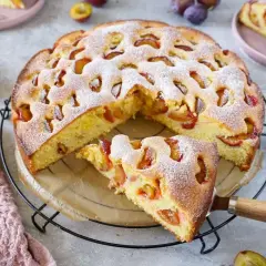 Saftiger pflaumenkuchen mit gefrorenen pflaumen, bestäubt mit Puderzucker. Ein Stück wird gerade herausgenommen.