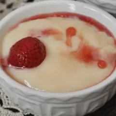 Pyszny krem cukierniczy z truskawką i sosem malinowym w białej miseczce.