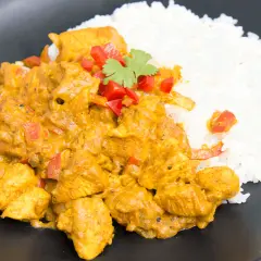 Aromatyczny kurczak curry z ryżem, doprawiony papryką i świeżą kolendrą, podany na czarnym talerzu.