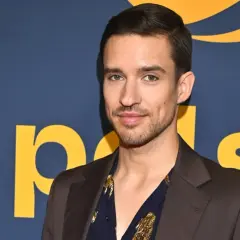 Dominik Smaruj w eleganckim garniturze i wzorzystej koszuli pozuje na tle niebieskiego baneru z żółtymi literami.
