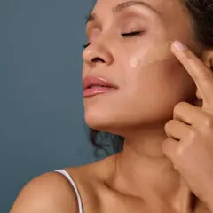 Application d'un fond de teint pour un maquillage teint parfait. Une femme applique délicatement le produit sur sa joue.