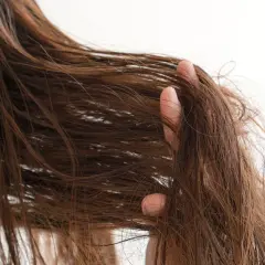 Braune Haare, die sich strohig und trocken anfühlen, werden von einer Hand durchkämmt.