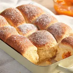 Frisch gebackene Buchteln, bestäubt mit Puderzucker, warten darauf, mit Marillenmarmelade gefüllt zu werden. Ein echtes Buchteln original Rezept.