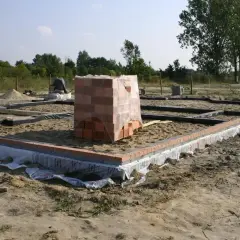 Stan zero budynku: fundamenty z cegły i betonu, stos materiałów budowlanych.