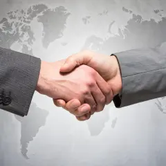 Uścisk dłoni dwóch mężczyzn w garniturach na tle mapy świata. Symbolizuje globalne partnerstwo i ddp.