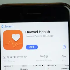 Ekran telefonu z aplikacją Huawei Health. Ikona serca z pulsem, przycisk "GET". W tle pomarańczowy przedmiot.