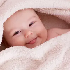 Uśmiechnięta Aurelia wtulona w miękki kocyk, wystawia języczek.