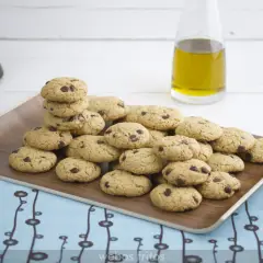 Montón de galletas caseras de pueblo con chispas de chocolate en una bandeja de madera, junto a una botella de aceite de oliva.