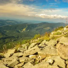 Kamienista ścieżka na Babiej Górze, z widokiem na zielone doliny i malowniczą miejscowość w oddali.