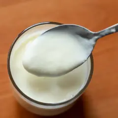 Łyżka z jogurtem greckim nad szklanką.
