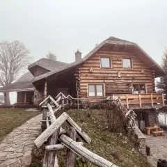 Drewniany dom w stylu góralskim, otoczony mgłą, zaprasza do odpoczynku w Beskidzie Wyspowym. Kamienna ścieżka prowadzi do przytulnego schroniska.