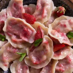 Pyszne pierogi z truskawkami, ozdobione świeżymi owocami i miętą, prezentują się apetycznie na talerzu.
