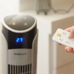 Mano con control remoto ajustando el ventilador para una temperatura ideal para dormir. El display muestra 27 grados.