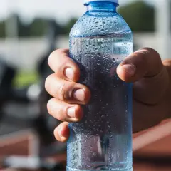 Main d'un sportif tenant une bouteille d'eau fraîche, idéale pour boire de l'eau avec du sel après l'effort.
