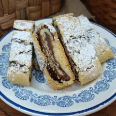 Fette di biscotti della nonna con ripieno di crema al cioccolato, spolverati di zucchero a velo, su un piatto decorato.