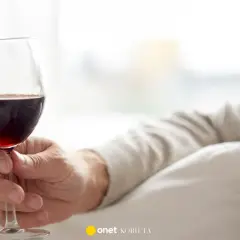 Dłoń trzyma kieliszek czerwonego wina. Czy czerwone wino obniża ciśnienie? Warto to sprawdzić.