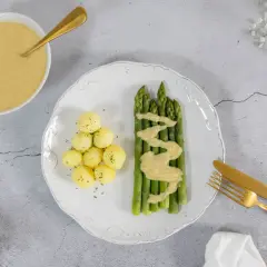 Spargel mit kleinen Kartoffeln und einer cremigen, veganen Sauce Hollandaise. Ein goldener Löffel liegt bereit.